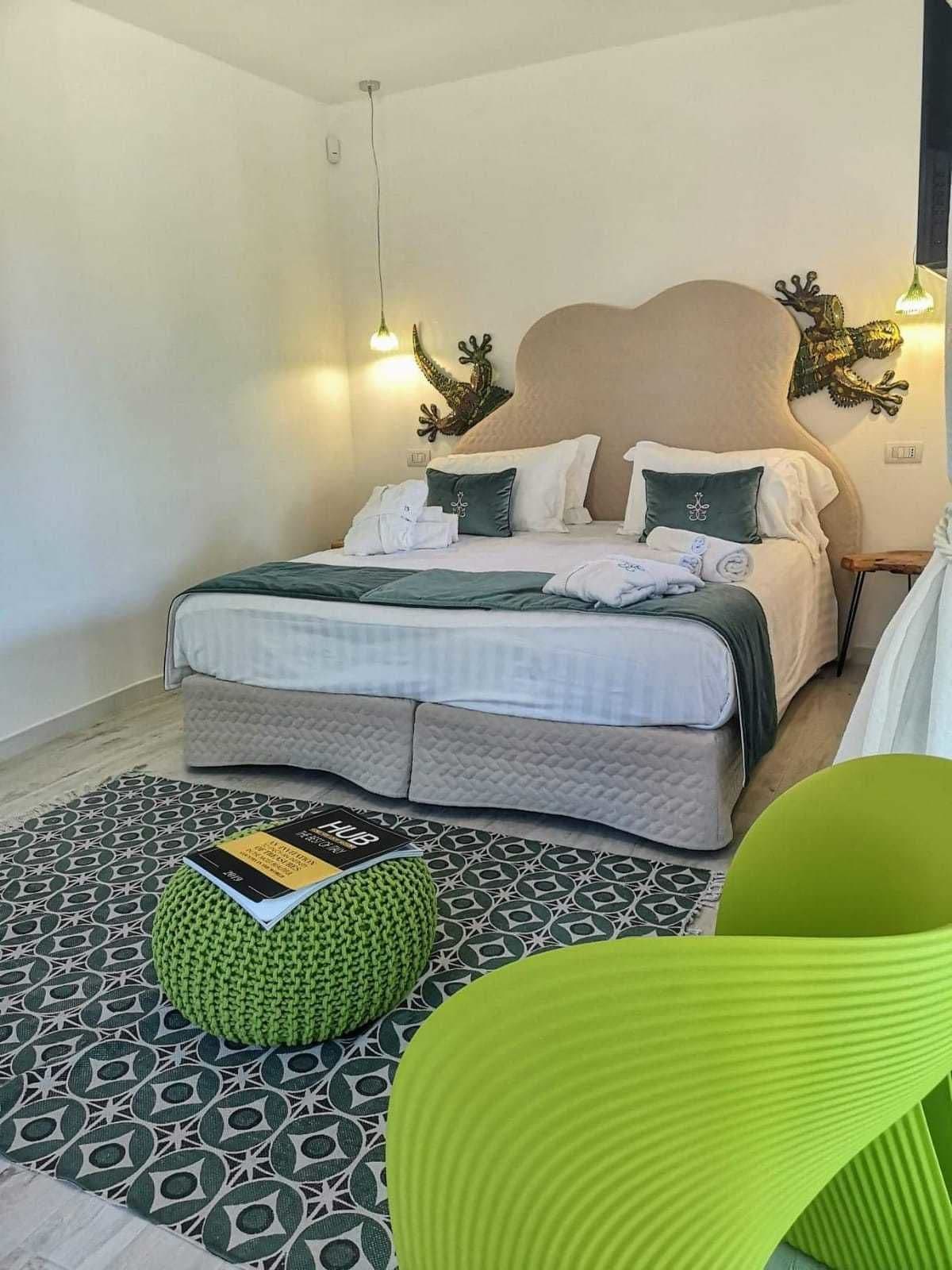 A bedroom with a bed, a green pouf, a patterned rug, and a green chair.