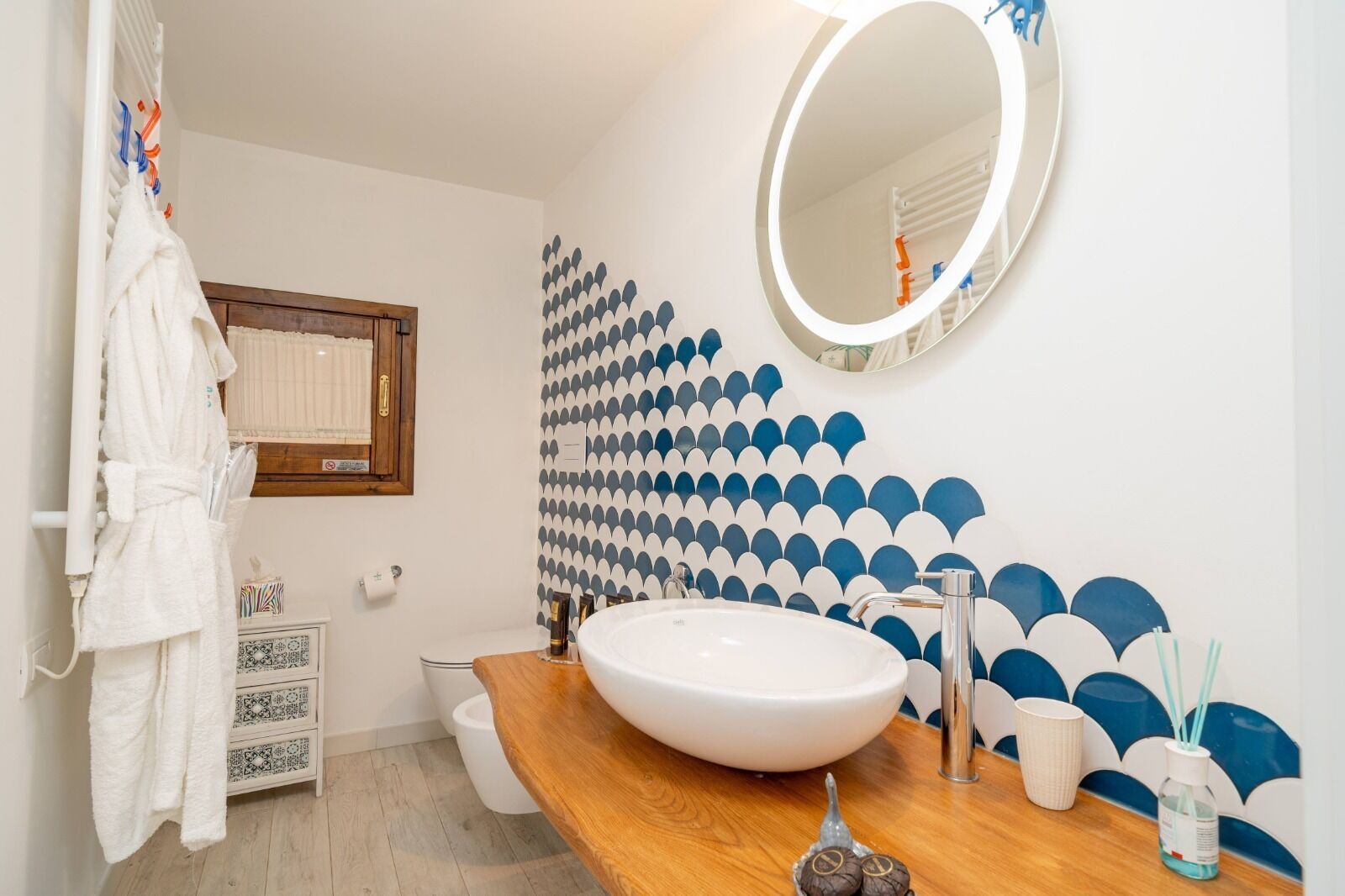 A bathroom with a wooden vanity, a large mirror, a white sink, and a patterned wall.