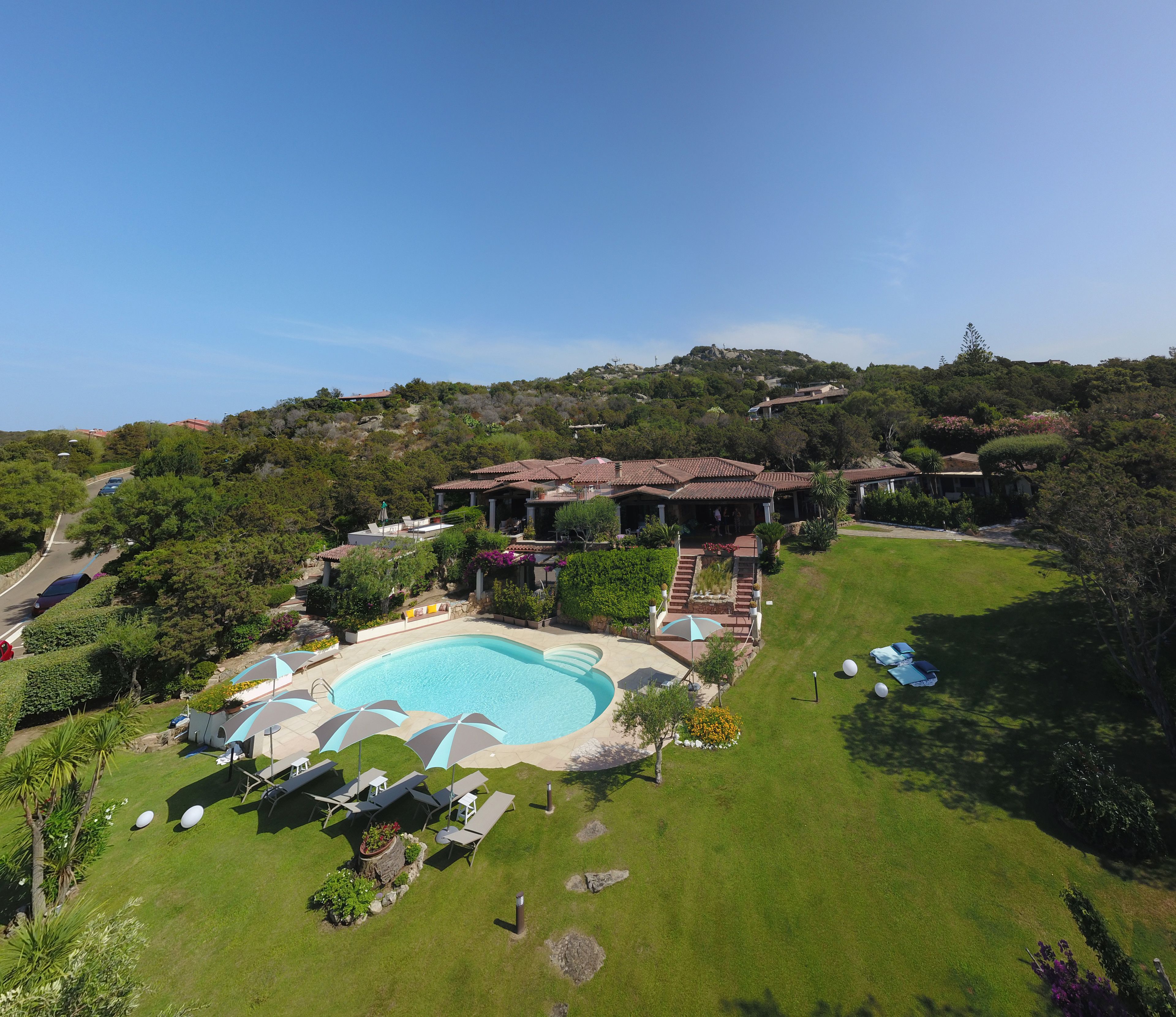 A large swimming pool surrounded by lounge chairs and umbrellas, with a hillside in the background.