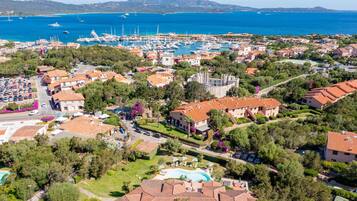 Vista aérea de un pueblo costero con un puerto deportivo, edificios residenciales y una piscina.
