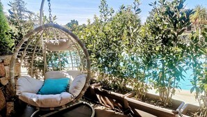 Una poltrona sospesa con cuscini, una piscina e piante in vaso in un giardino.