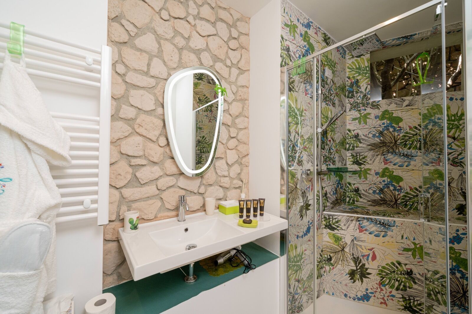 A bathroom with a stone wall, a white sink, a mirror, and a shower with a floral tile design.