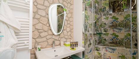 Un baño con pared de piedra, un lavamanos blanco, un espejo y una ducha con diseño de azulejos florales.
