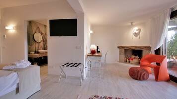Ein modernes Hotelzimmer mit einem Bett, einem kleinen Tisch, einem Sessel, einer Couch, einem Kamin und einem an der Wand befestigten Fernseher.