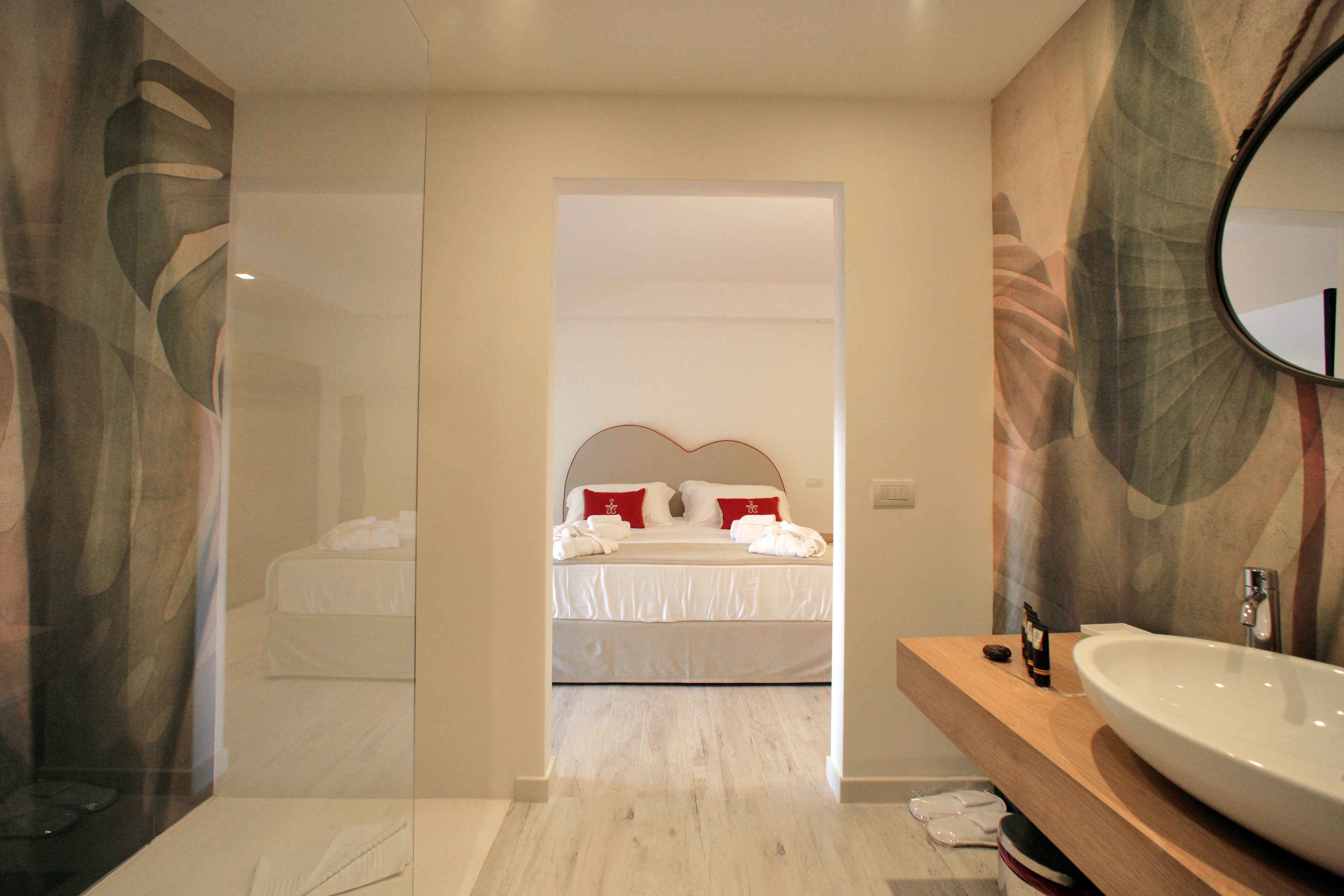 A modern hotel room with a large bed, a bathroom with a large sink, and a mirror.