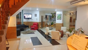 Un vestíbulo de hotel con una escalera, un televisor de pantalla plana, una recepción y un área de comedor.