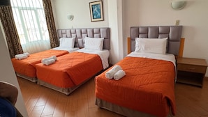 Habitación de hotel con dos camas, cada una con colcha naranja y almohadas blancas. Se observa un cuadro en la pared, una ventana con cortinas y una mesita de noche con lámpara.