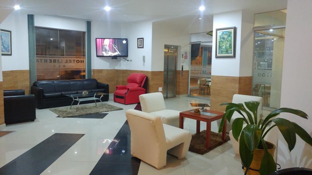 A hotel lobby with a black leather sofa, a red armchair, a white armchair, a small table, and a potted plant.
