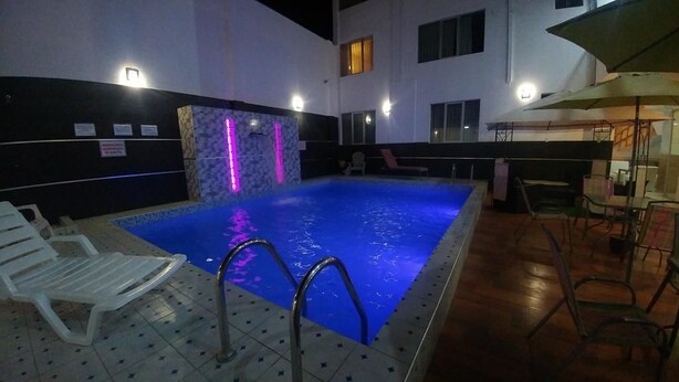 Una piscina interior con suelo de baldosas, pared de piedra con fuente de agua y zona de bar con sillas y sombrillas.