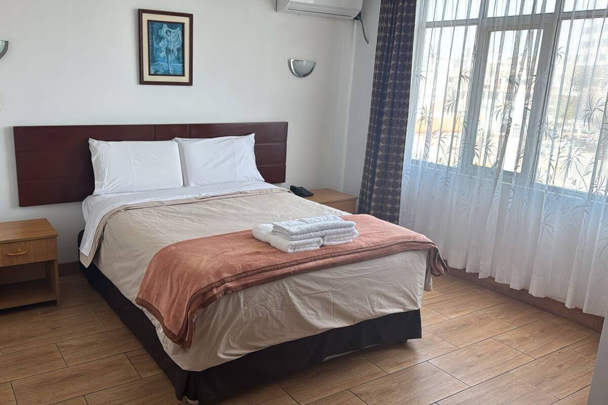 A neatly made bed with white and brown linens, a wooden nightstand, and a framed picture on the wall.