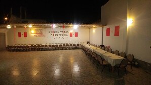 Un amplio salón de banquetes interior con filas de mesas y sillas, suelo de baldosas y un cartel del Hotel Libertad.