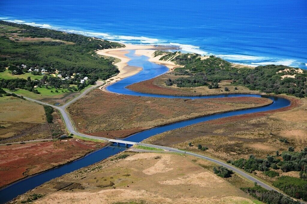An aerial view of a coastal area with a winding river, a bridge, and a beach.
