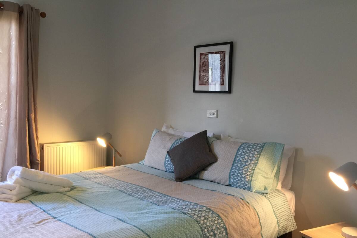 A neatly made bed with a patterned bedspread, a framed picture on the wall, and bedside lamps.
