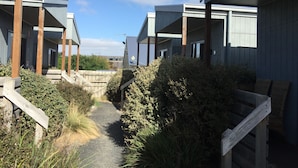 A pathway leading to modern buildings with wooden railings and a clear sky. - Kilcunda Ocean View Motel (Kilcunda)