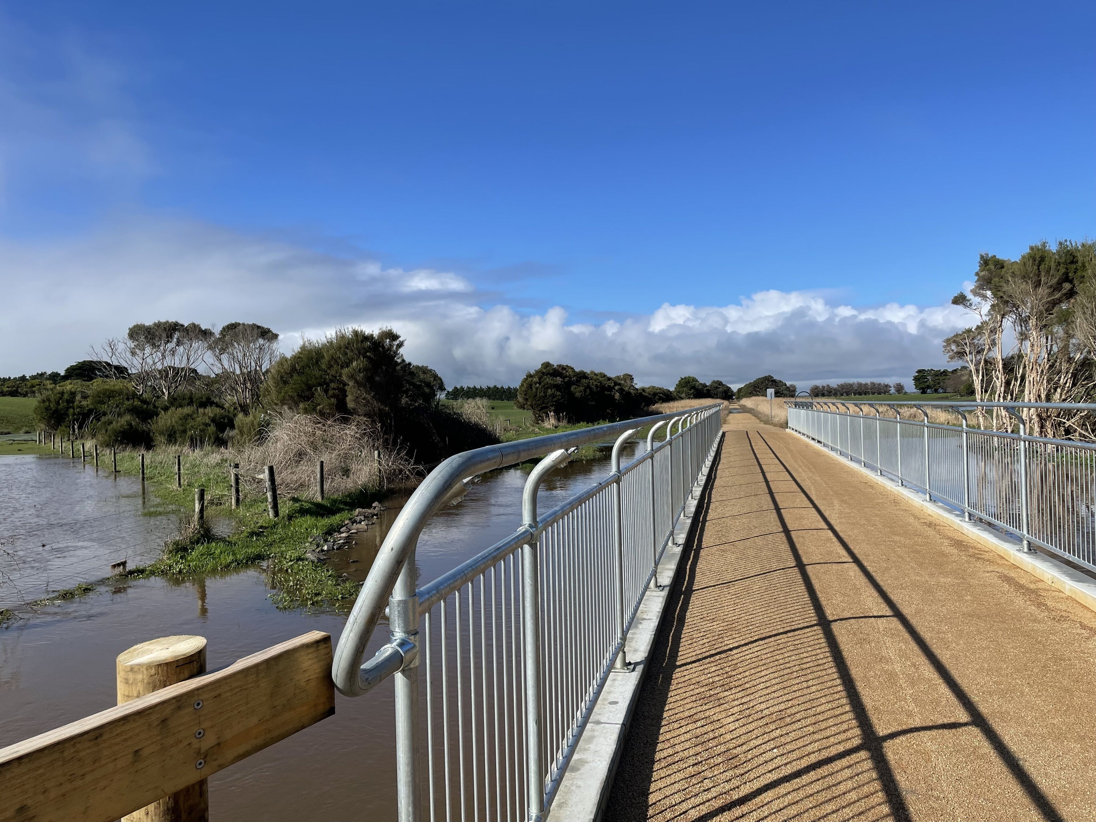 A pedestrian bridge over a water body with metal railings and a wooden walkway.