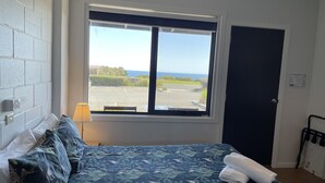 A bedroom with a bed, a window with a view of the outdoors, a door, and a lamp. - Kilcunda Ocean View Motel (Kilcunda)
