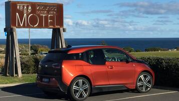 Um carro vermelho estacionado em frente a um letreiro de motel, com vista para o oceano.