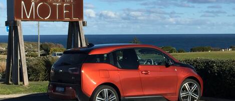 A red car parked in front of a motel sign with a view of the ocean.