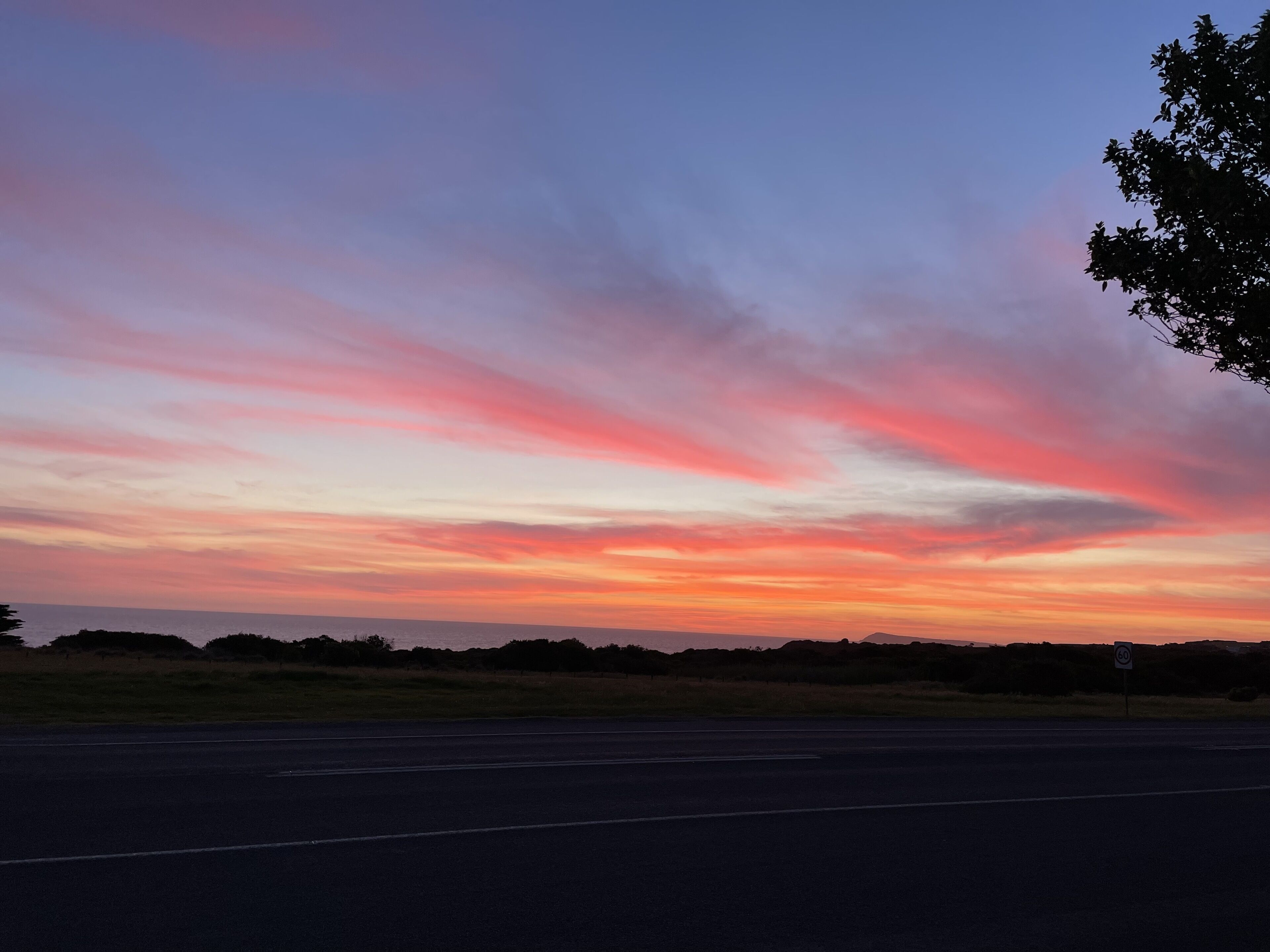 A sunset over a flat landscape with a road and a speed limit sign.