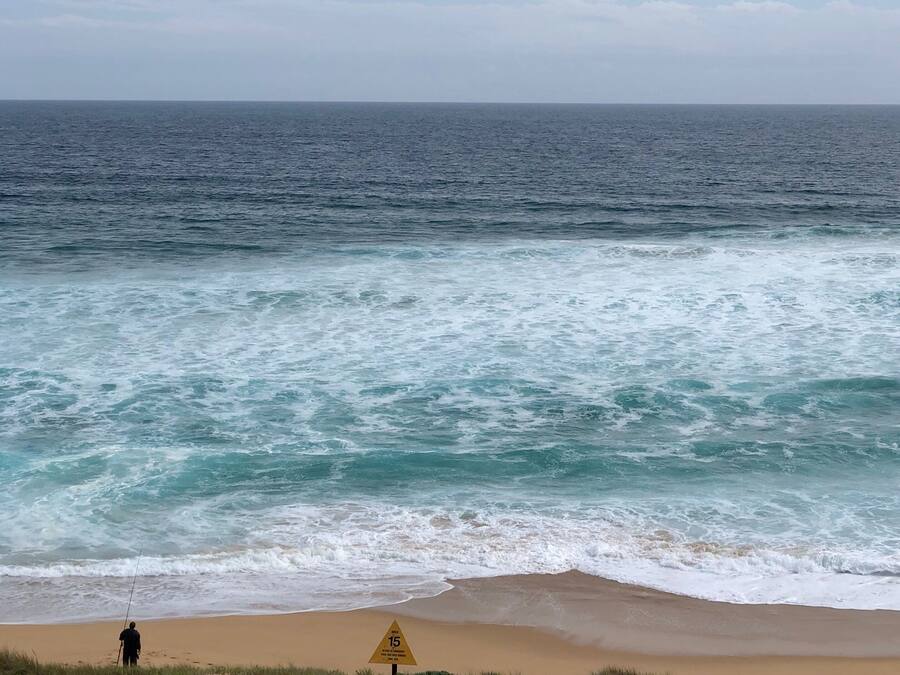A beach with a warning sign and a person fishing.