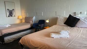 A hotel room with two single beds, a chair, a desk, a lamp, and a framed picture on the wall.