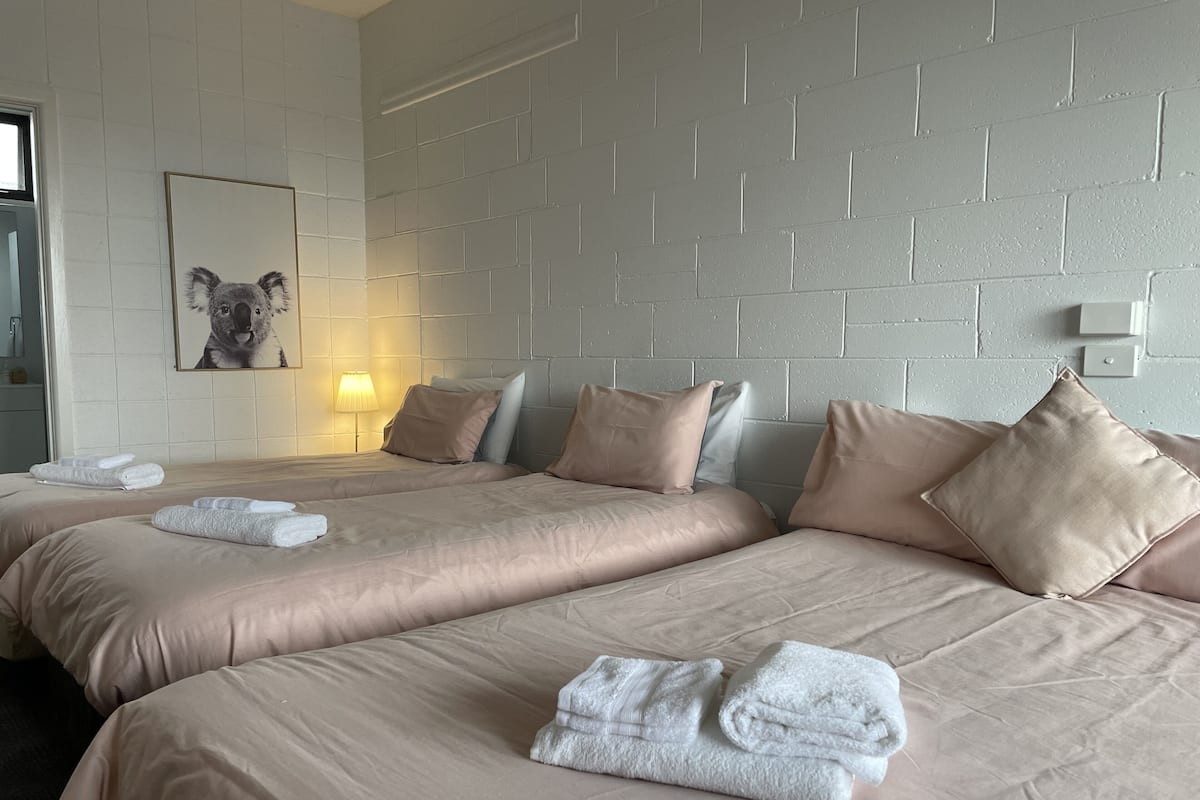 A hotel room with two beds, beige bedding, and a wall-mounted picture of a koala.