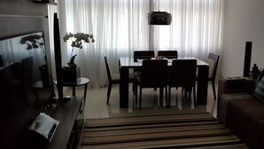 Uma sala de estar com uma mesa de jantar, cadeiras, um sofá, uma televisão e uma planta.