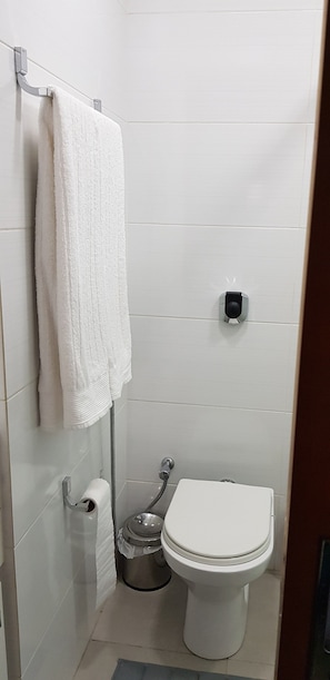 Une petite salle de bain blanche, équipée de toilettes, d’un porte-serviettes et d’un distributeur de serviettes en papier.