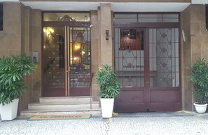 L’entrée d’un hôtel, avec une porte en bois sombre, des panneaux de verre et une enseigne indiquant « ENTRÉE SERVICE ».