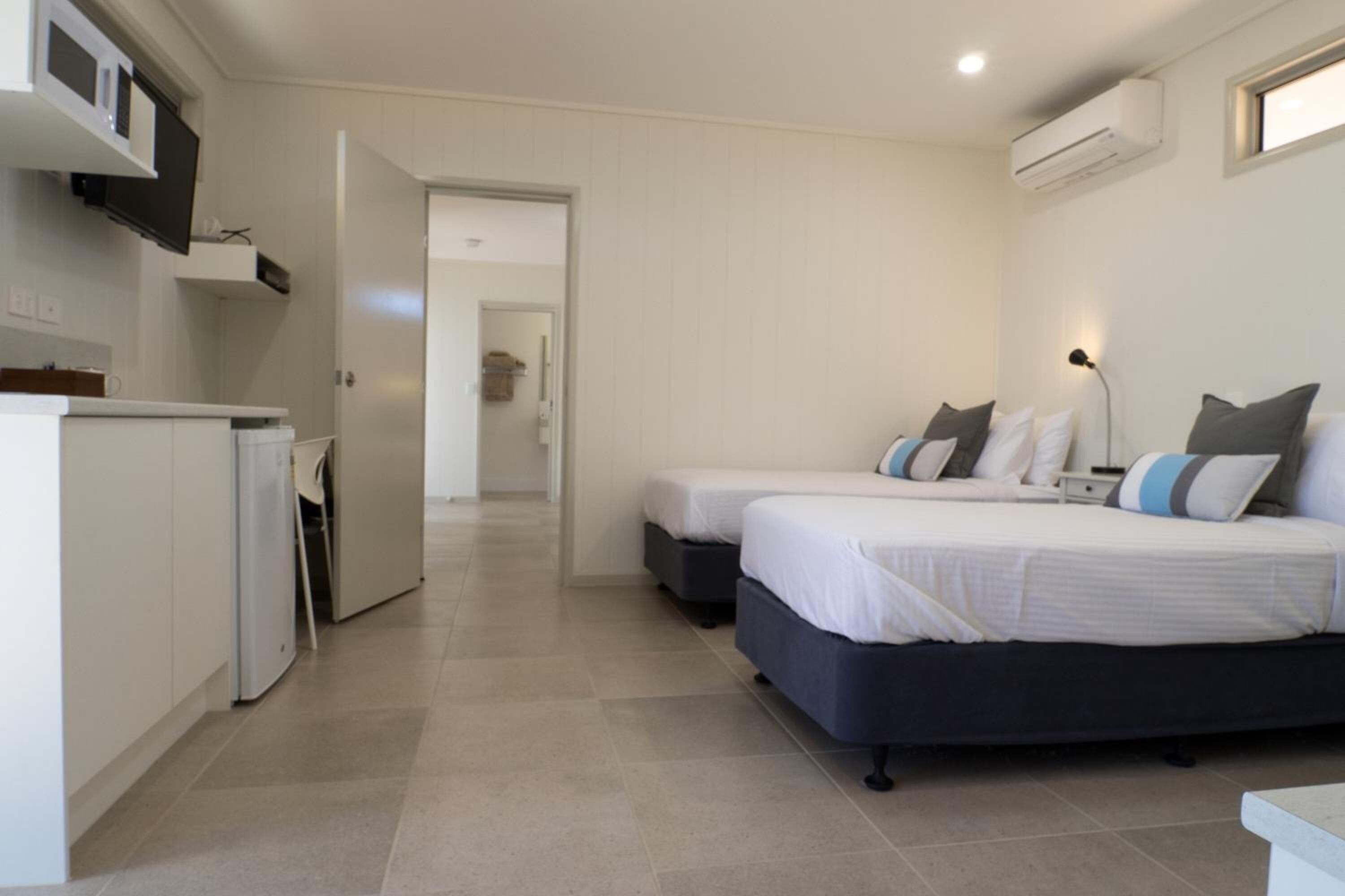 A bedroom with two beds, a kitchenette, and an air conditioning unit.