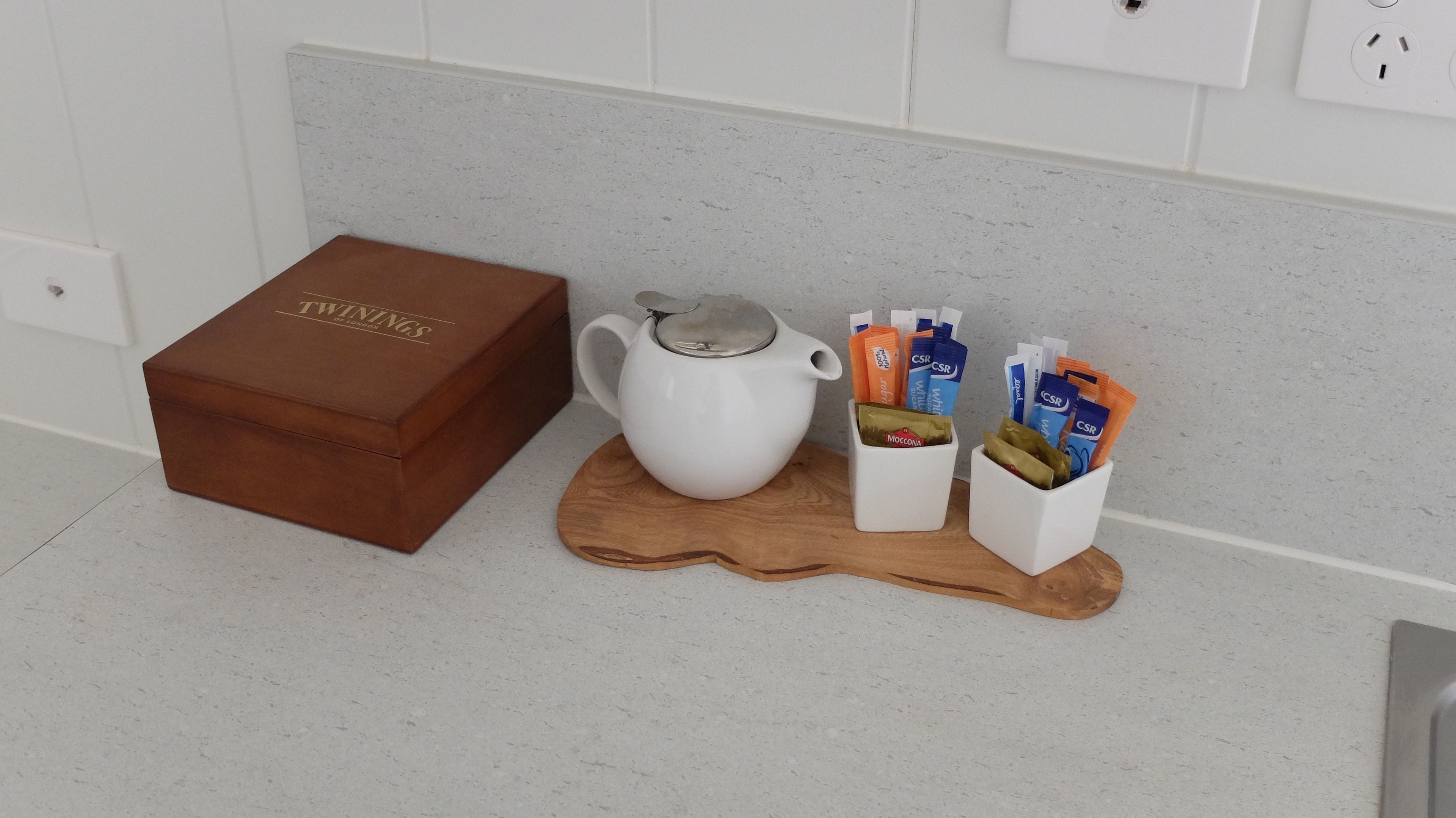 Una encimera de cocina con un hervidor blanco, una caja marrón y dos recipientes blancos con alimentos.