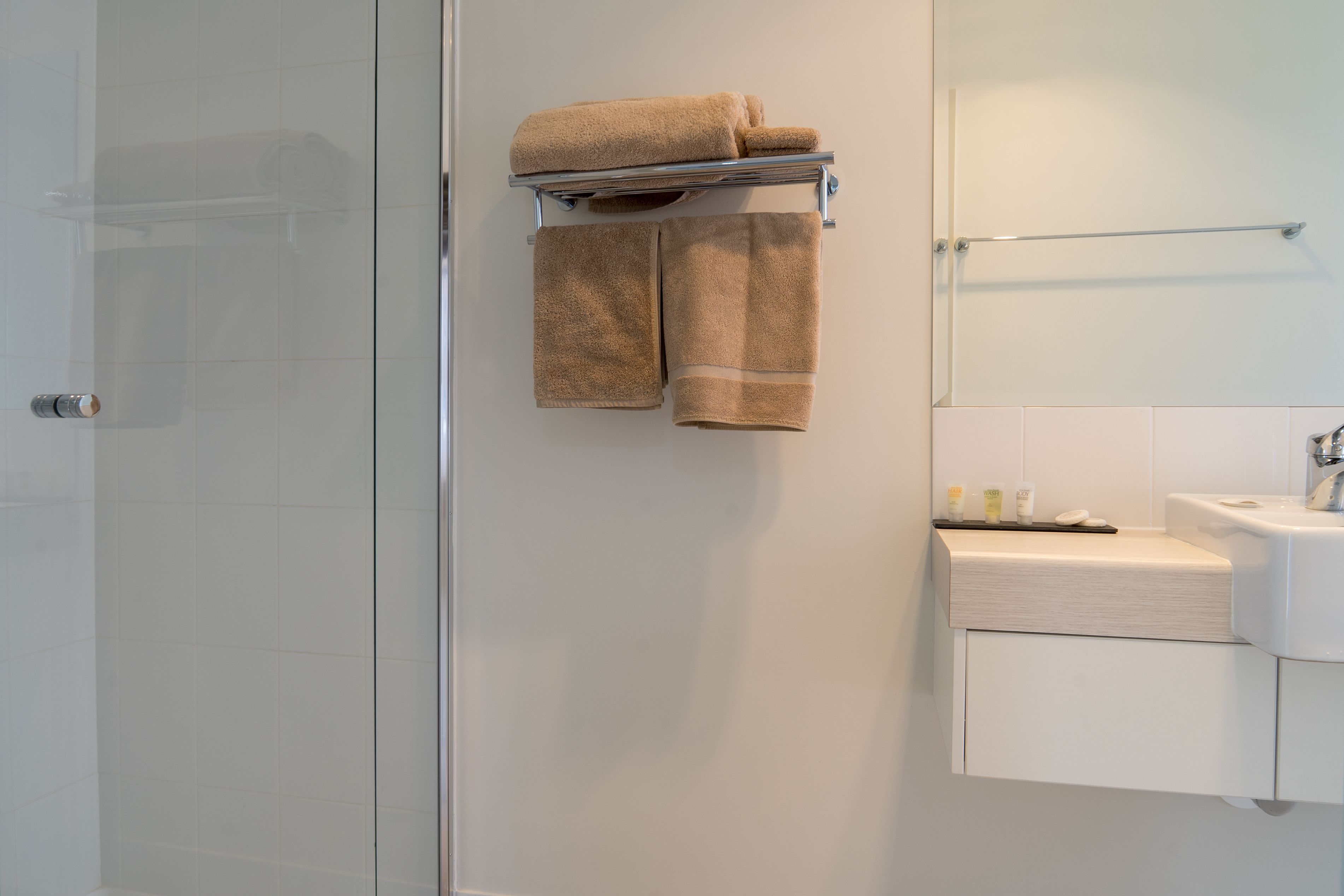 A bathroom with a glass shower door, a towel rack with two towels, a sink, and a mirror.