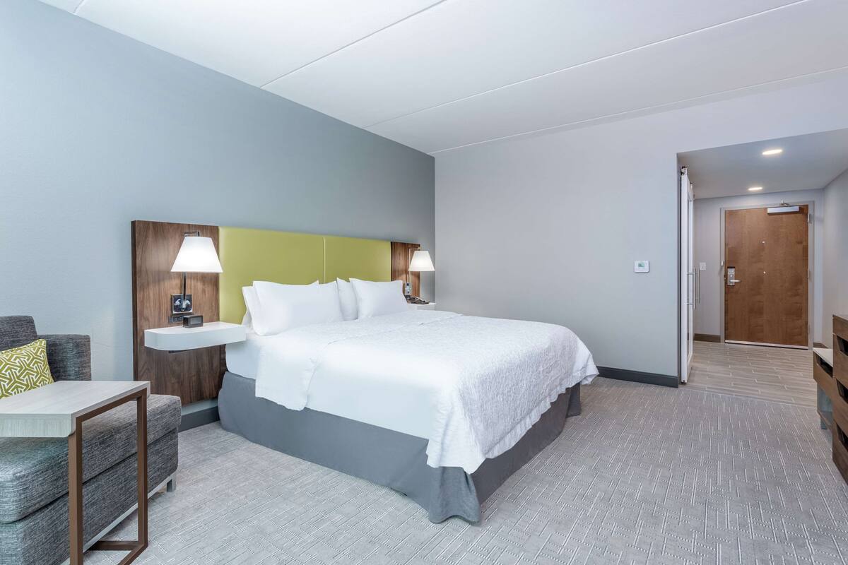 A hotel room with a large bed, bedside tables, a chair, and a wooden door.