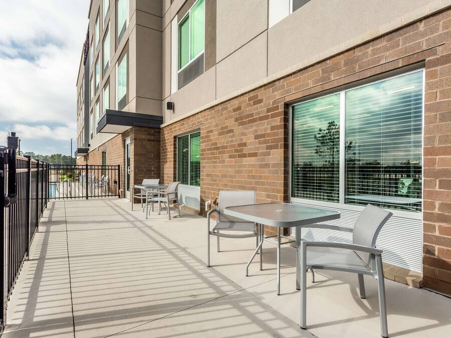 An outdoor patio area with a brick wall, large windows with blinds, and outdoor seating.