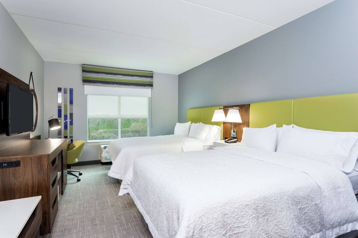 A hotel room with two beds, a desk, a TV, and a window with a view.