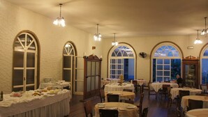 Un restaurante con varias mesas redondas, ventanas arqueadas y candelabros.