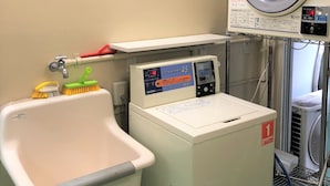 A compact laundry room with a front-loading washing machine, a sink, and a drying machine. - Simple Hotel Kyoei (Yokohama)