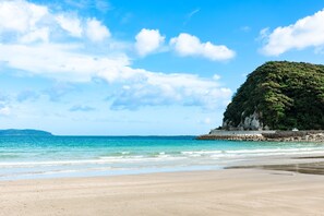Une plage à l’eau turquoise et limpide, un rivage sablonneux et une falaise rocheuse parsemée de végétation.