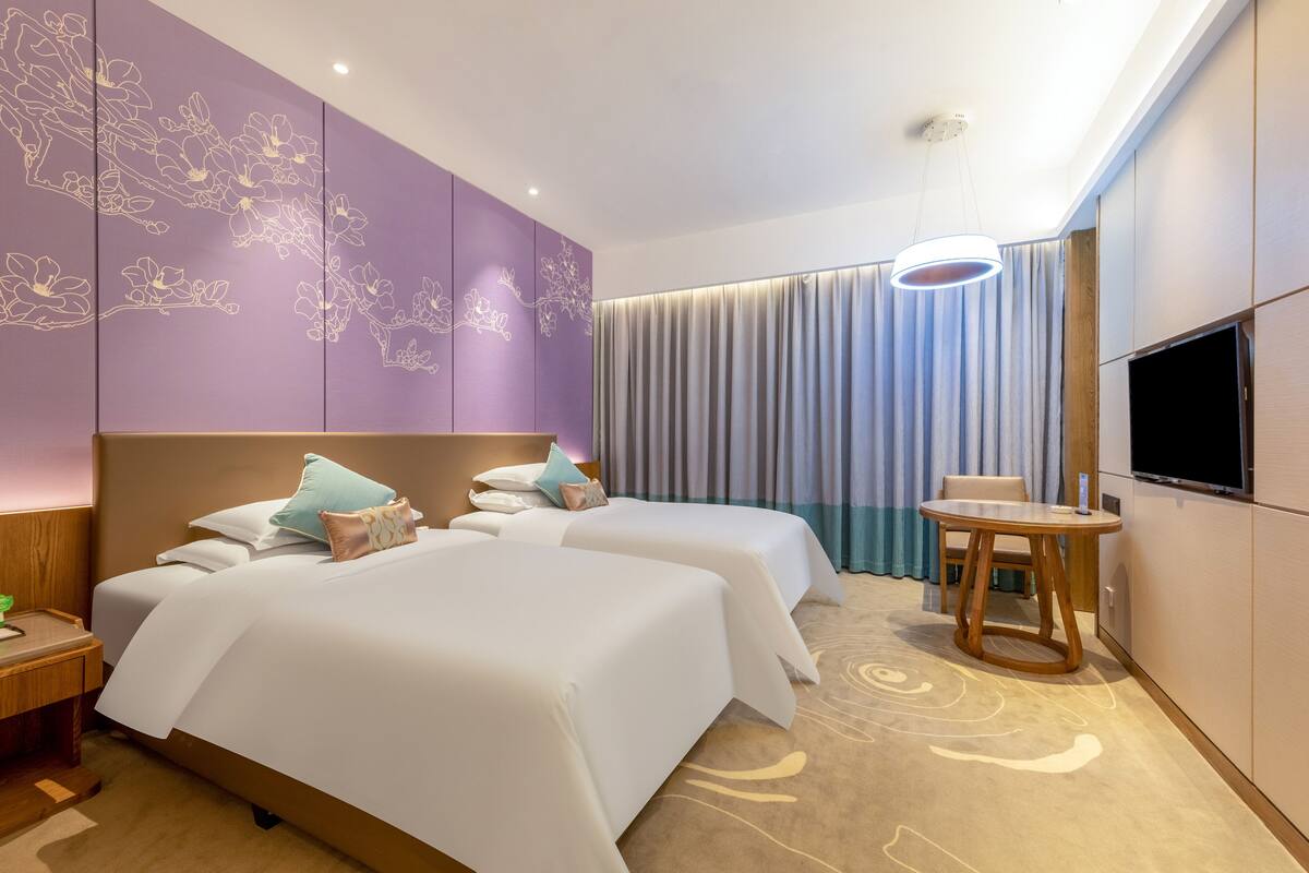 Habitación de hotel con dos camas, televisión, una mesita y cortina.