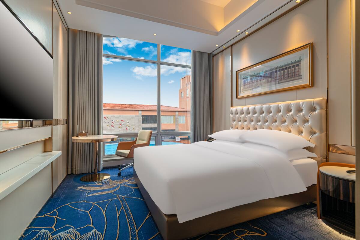 Habitación de hotel con una cama grande, televisión, una mesita redonda y vistas a la ciudad.