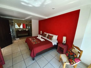 Une chambre d’hôtel avec un mur d’accent rouge, un grand lit recouvert d’une courtepointe rouge, une chaise en bois et une petite table avec une lampe.