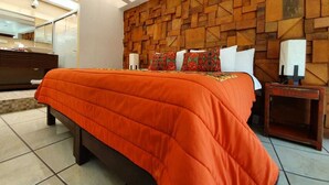 A modern hotel room with a geometric patterned wall, a large bed with an orange bedspread, and a nightstand with a lamp.