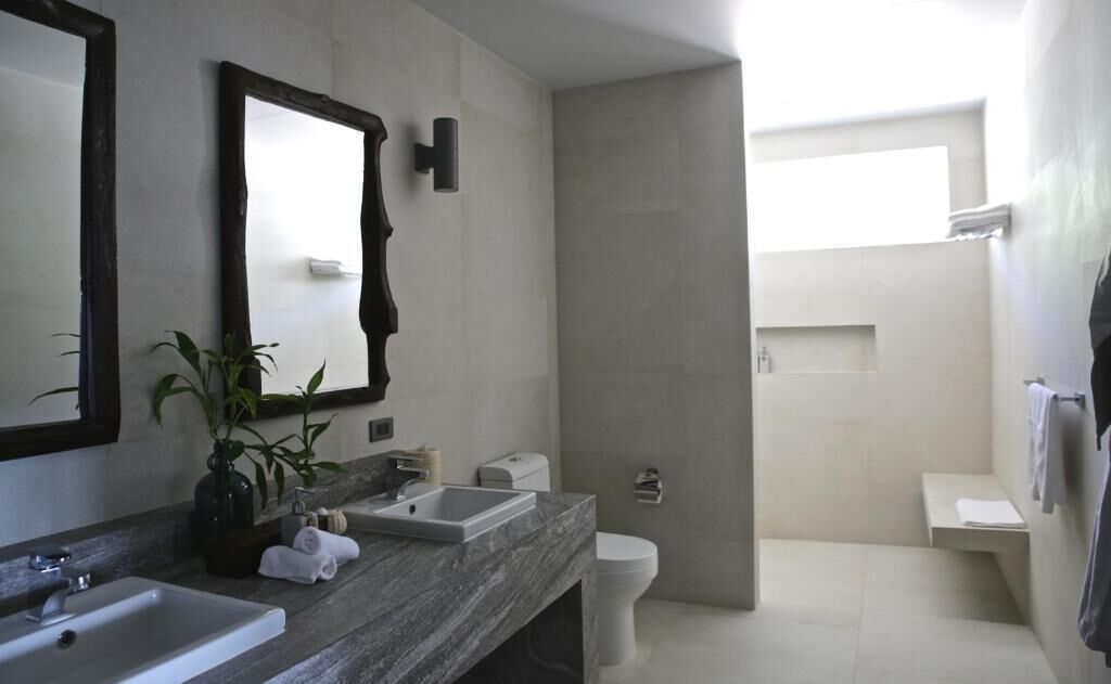 A modern bathroom with a large mirror, two sinks, a toilet, and a shower area.