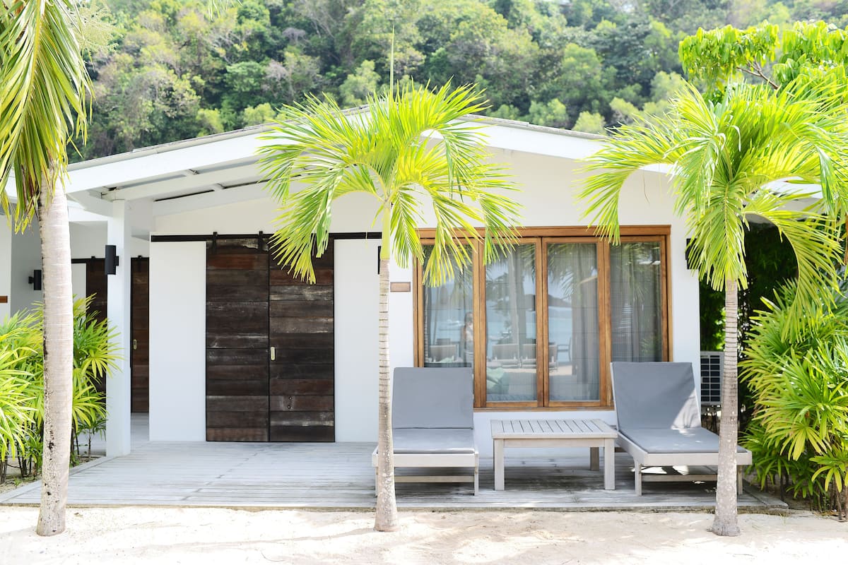 A modern building with a covered patio, two lounge chairs, and several palm trees.