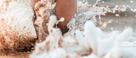 A close-up of a person's feet stepping into a sandy beach with water splashing around.