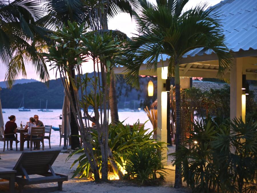 Un restaurante frente al mar con terraza al aire libre, palmeras y vistas al océano.