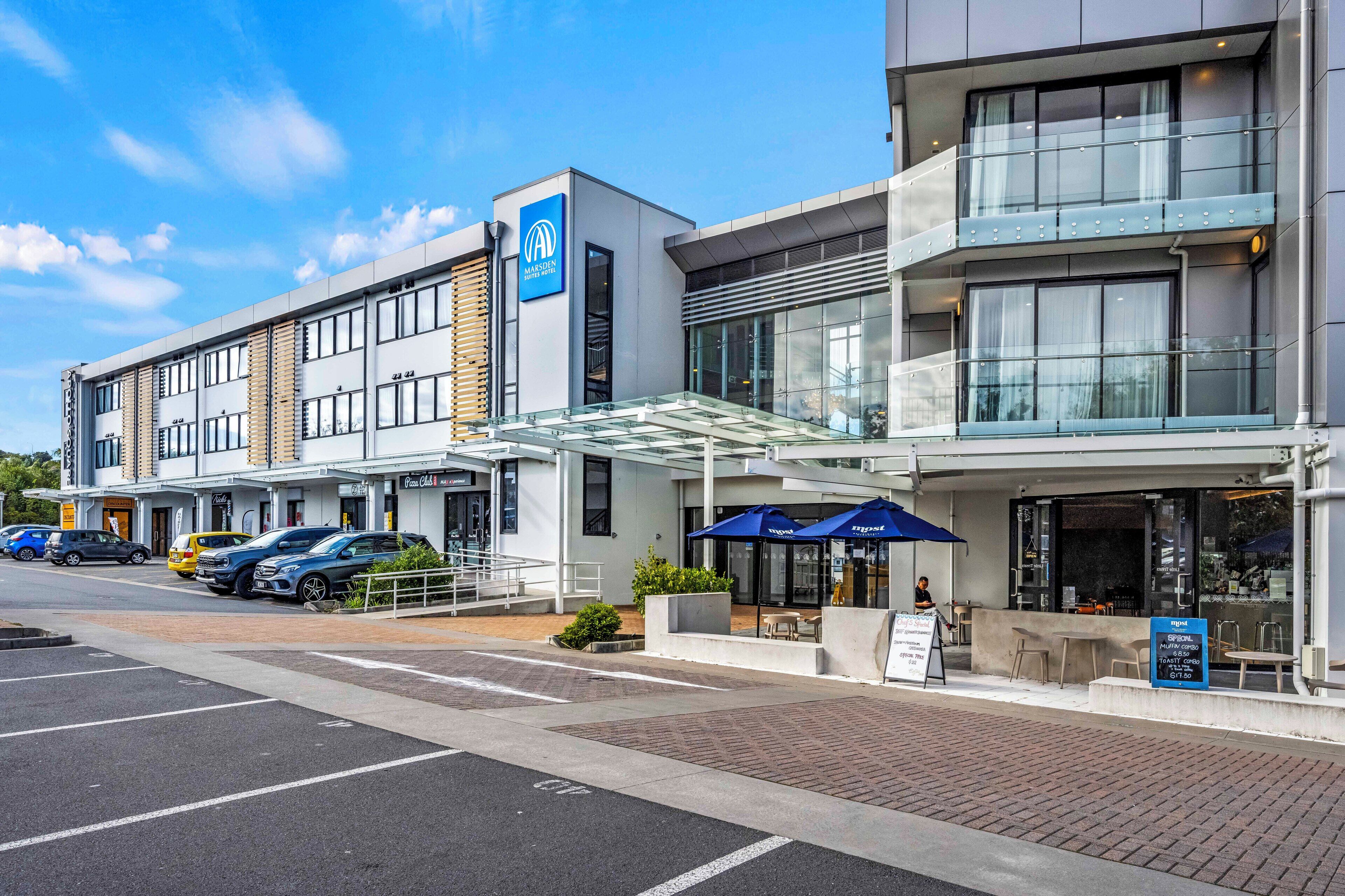 Un hôtel moderne doté d’une façade en verre, d’une terrasse et d’un parking.