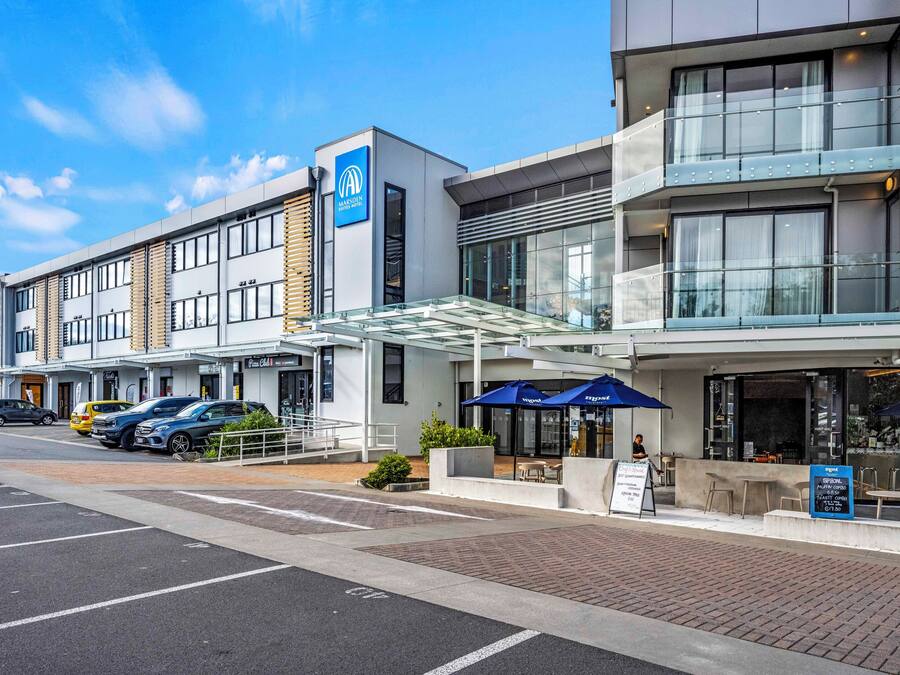 Un hôtel moderne doté d’une façade en verre, d’une terrasse et d’un parking.