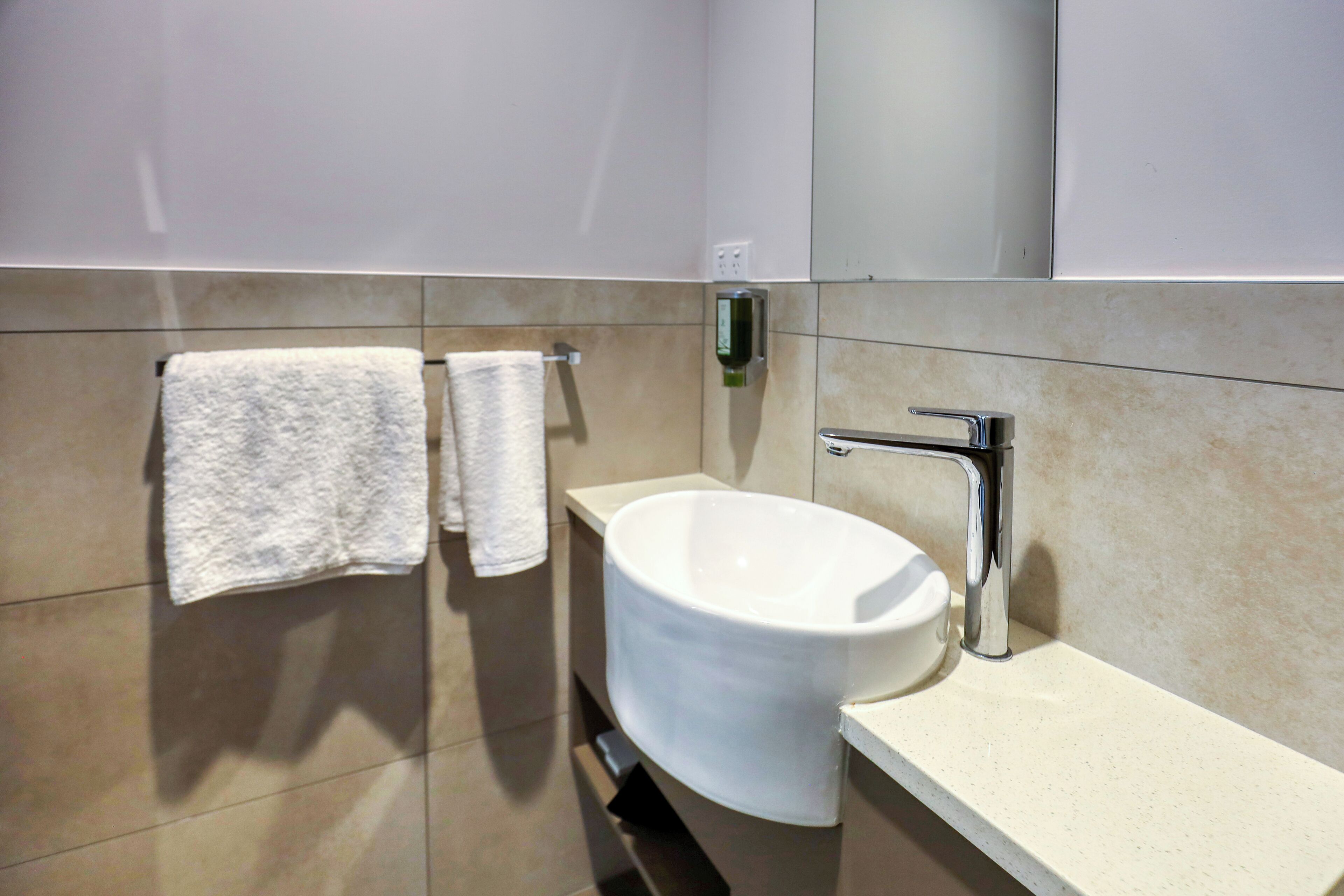 Un baño moderno con un lavamanos blanco, dos toallas y un espejo.