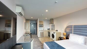 Una habitación de hotel moderna con una cama grande, un escritorio, una lavadora y una kitchenette.